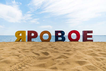 multicolored inscription Yarovoe in russian language on the yellow sand on the background of the lake and tourists. Yarovoe name of the resort town in the Altai territory.の写真素材