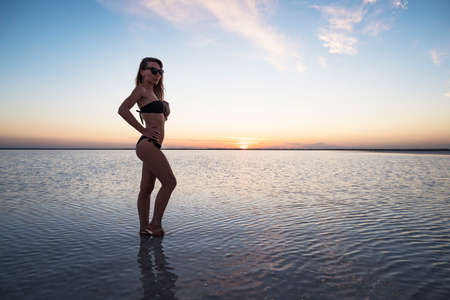 Salt lake. Girl standing in the water at sunset. A young woman stands alone in a beautiful landscape and looks away. reflection in the water. copy spaceの写真素材