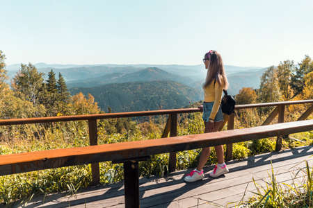 A young girl looks at the beautiful nature. to enjoy the scenery. Sexy woman in short shorts on a bridge in the mountains. Country walks in the countrysideの写真素材