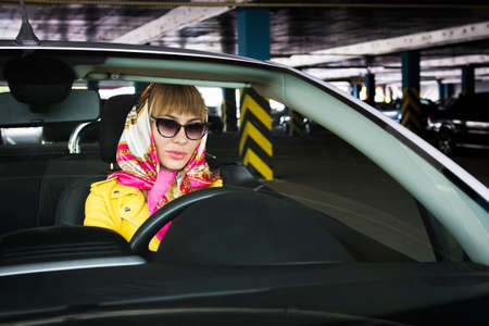 one glamorous brutal blonde woman sit in cabriolet car, glamour girl inside cabrio auto. Space inside dark underground parking . Fashionable girl driver looks at the camera.の写真素材