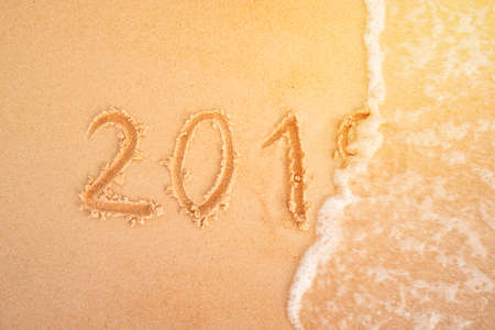 2019 figures on sandy beach in the background New Year's Eve. The sea wave washes away the inscription 2019 on the yellow sand close-up. New year holidays on the beach.の写真素材