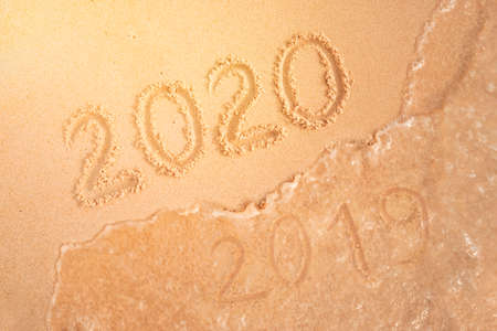 number of the new year written in sand, on tropical beach. Change numbers 2019 to 2020. New year holidays on a tropical island. The sea wave washes away the inscription 2019.の写真素材