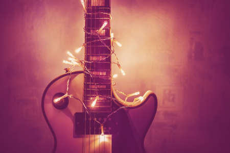 white jazz guitar and christmas decorations on the dark background. Electric guitar with lighted garland on dark background. Gift guitar classic shapes for Christmas or new year.の写真素材