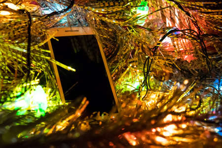 Christmas toys and white smartphone in glowing Christmas lights. Blank screen for photo or text. copy spaceの写真素材