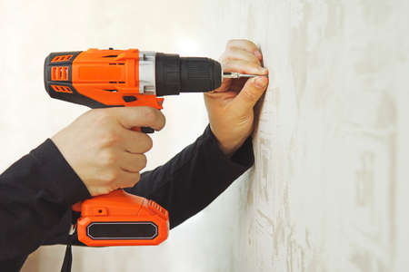 Concept. Worker is screwing the drywall screw by screw gun to the plasterboard wall in apartment is under construction, remodeling, renovation, overhaul, extension, restoration and reconstructionの写真素材