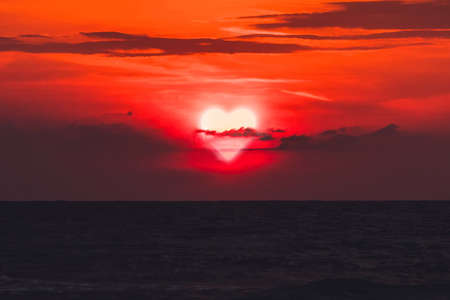 cloud heart. Heart walks off into the sunset over the sea in dark clouds. Past love. Separation. concept. Sun is the heart is the evening before sunset. Valentine's dayの写真素材