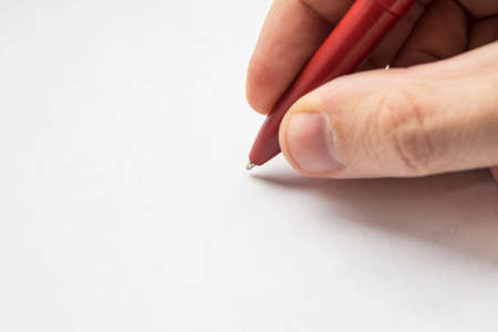 right hand with pencil and left empty over a white blank sheet of paper lying on table. empty space for design. Red pen in hands close upの写真素材