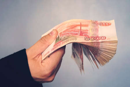 a lot of money in the hand of a young businessman on a blue background. A stack of banknotes of Russian rubles with a face value of 5000 rubles. successful businessmanの写真素材