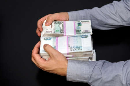 Anonymous businessman reaching out hand to grab money, Russian ruble currency, in dark room. Male...