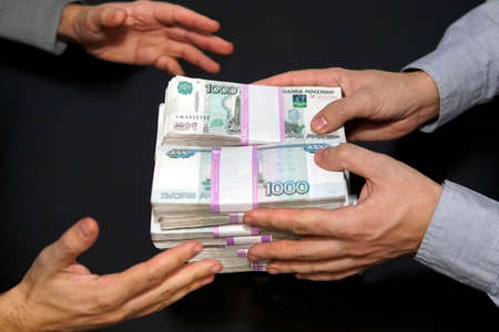 A million rubles in men's hands. Bribery in Russian rubles in a dark room. The concept of corruption and bribery. One man gives money another takes it. A good financial deal. cash saleの写真素材