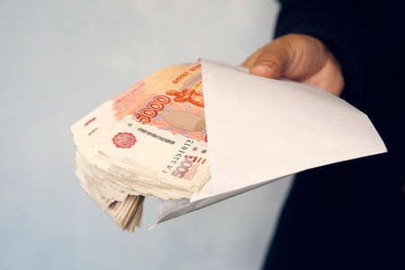 Large denominations of 5000 rubles in a white envelope. A man hand holds an envelope with money. the concept of bribery and corruption. cash, cashflowの写真素材