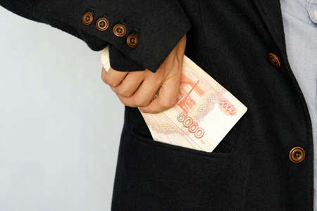 Bearded businessman in dark suit removes russian rubles banknotes to his suit pocket . Financial theme. man put bills in his pocket. Salary.の写真素材