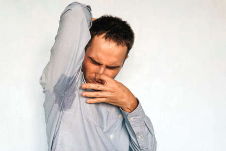 adult guy held his nose with his hands while feeling the unpleasant smell from underarms. Businessman sweating excessively smelling bad in office at workp. Copy spaceの写真素材