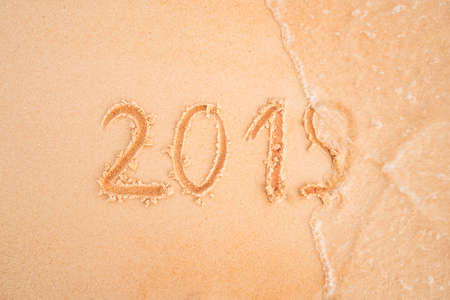 Years 2019 are inscribed on sandy beach on the yellow sand close-up. sea wave washes away the inscription 2019. The concept of year change.の写真素材