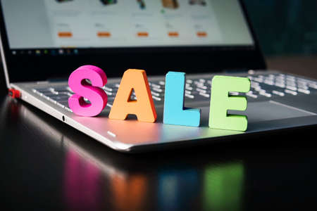 Big colored letters SALE set on laptop. Sale in online shop concept. Opened notebook with wooden word SALE on keyboard over black table. Internet shopping. Buying discount things. E-commerce.の写真素材