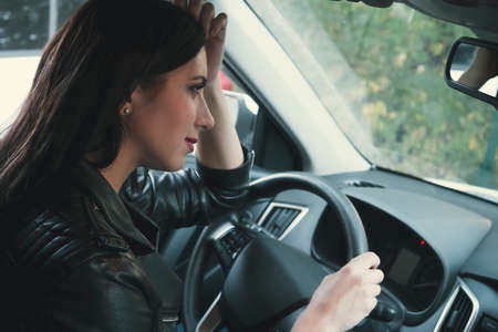 Side view of a cute young lady showing faint smile sitting inside car. Brunette woman driver stops...