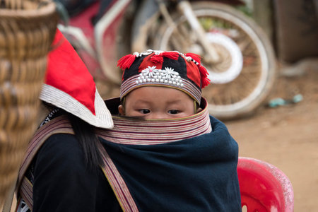 A small child in a bag behind a teenage girl. Red dzao - a small nation of North Vietnamのeditorial素材
