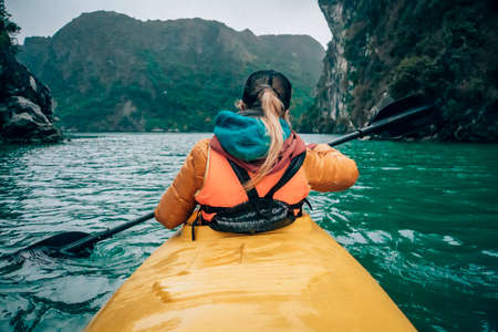 Girl kayaking on the seaside of Halong bay in Vietnam. Woman rowing oars in the boat. The view from the back.の写真素材