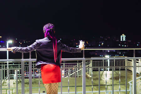 beautiful fashionable young woman with coffee in night city. a young woman drinks coffee through a straw from a disposable plastic Cup.の写真素材
