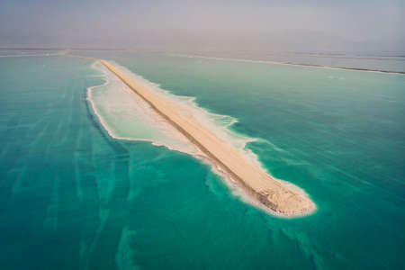 The southern part of the Dead Sea, is divided into pools from which extract minerals. The rocky shore is covered with white salt crystals washed by the blue waters of the dead sea.の写真素材