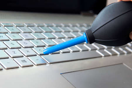 Closeup shot of female hand sweeping dust from laptop keyboard using air bulbの写真素材