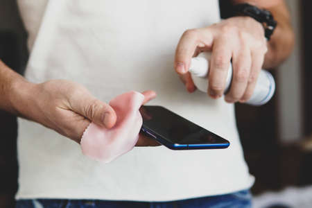 a man splashes on smartphone a sanitizer to disinfect and prevent viral diseases. Antibacterial...
