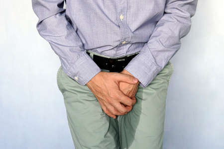 Urinary incontinence concept. Wet person. Blue background. adult man holds hands the groin area and trousers wet from urine. Health problem. Medical concept.の写真素材
