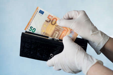 woman taking money out of female wallet wearing rubber gloves to prevent the spread of bacterias or viruses, take shopping during coronavirus pandemic. Microbes on money. Refusal of cash.の写真素材