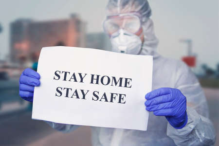 doctor in a protective suit at wear medical masks, holding paper with text STAY HOME STAY SAFE. stay at home in self-isolation policy campaign to control COVID-19 Coronavirus outbreak situation. warnの写真素材