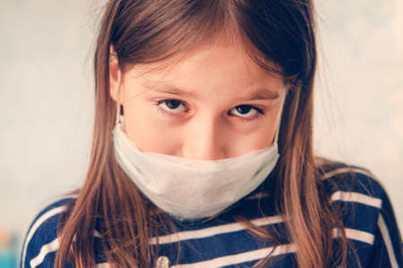A young pretty girl put on a medical mask. Portrait of a child in a protective mask on a blue background. sad emotion on his face.の写真素材