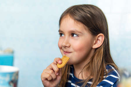 Young girl eating cookies on blue background sitting in the kitchen at home. Harmful but delicious...