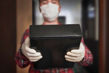 home delivery, online order. A man in a medical mask and rubber gloves with black box, a parcel in his hands. delivery during the quarantineの写真素材