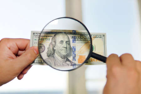 two dollar bill and magnifying glass isolated on white. men's hands hold 20 dollars and a magnifying...