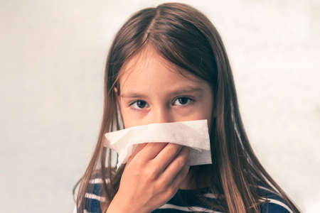 caucasian little girl to blow her nose with hygienic wet wipe. Seasonal sickness. child sneezes into a rag. sneeze cough and blow your nose in a napkin close-up.の写真素材