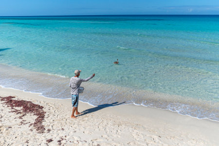 Varadero, Cuba. November 24, 2019: An old man feeds a large Pelican with fish on the shore of the Caribbean sea.のeditorial素材