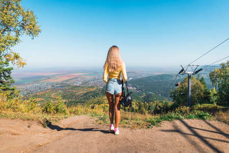 A tourist girl stands on the slope of the mountain Church and looks down on the resort town of Belokurikha. Altai Krai, Russia. Young sexy woman admiring the beautiful views of nature on mountain.の写真素材