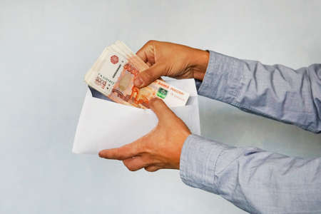 hand with rubles in the envelope against the supermarket shelves. Male hands consider rubles face value in 5,000 rublesの写真素材