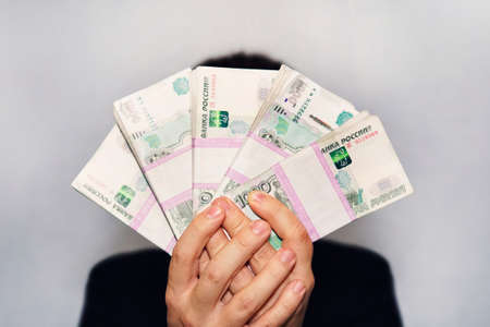 a lot of money in the hand of a young businessman on a blue background. A stack of banknotes of...