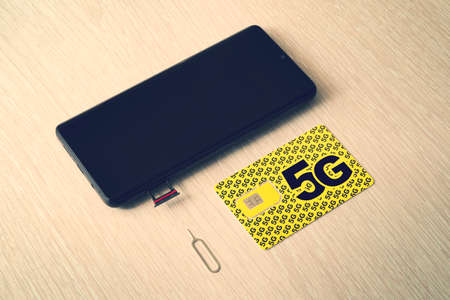 Broadband 5G mobile communication technology concept: SIM card tray, dual SIM card slot with two nano SIM cards on wooden background.の写真素材
