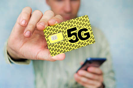 A man holds a yellow SIM card with the inscription 5G and a mobile phone in his hand. Replacing the...