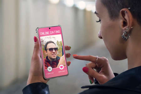A girl looks at smartphone photos of man in an online Dating app on street. touching on screen....