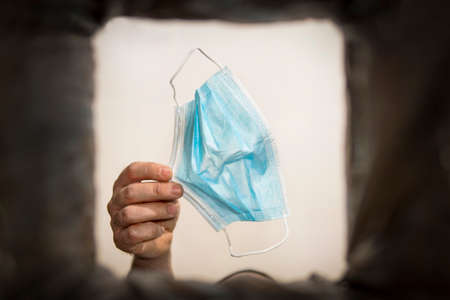 man's hand throws protective medical or surgical mask into the trash outdoors. Protection against...