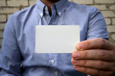 Business man handing a blank business card over background white brick wall on the street. plastic...