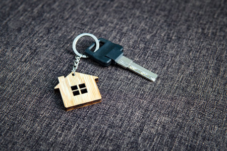 Close up of key with house-shaped key ring at dark sackcloth background. Concept of purchasing...