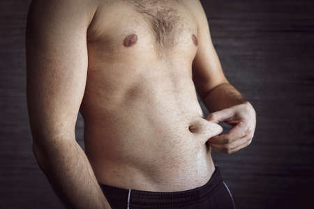 An adult male squeezes a fold of fat on his stomach. a man with a good figure squeezes the skin on his stomach.の写真素材
