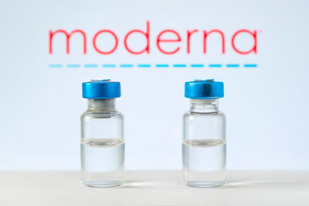 glass ampoule with a clear liquid on a blue background with the logo of a pharmaceutical company moderna. March 13, Barnaul, Russia.のeditorial素材