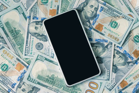 Dollar bills and smartphone, copy space, top view. blank black smartphone screen for text and design. the concept of accumulating profitability and earnings through a smartphone.の写真素材