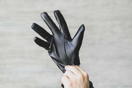 A man puts black leather gloves on his hands on a gray background. leatherette glovesの写真素材