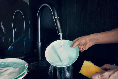 Male hand close-up washing a blue plate on dark background.の写真素材