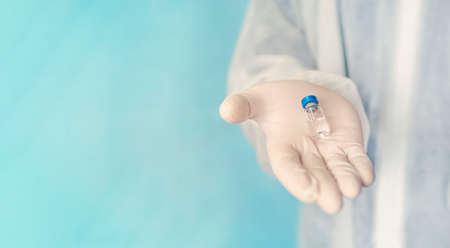 Vaccine in glass vial bottle, medicine liquid in doctor hand in glove. Vaccination injections as treatment on blue background.の写真素材